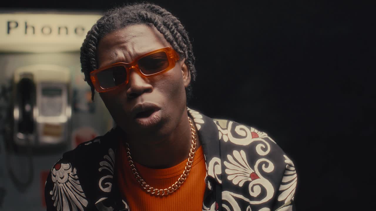 African American Man Performing Rap against Payphone in City Street