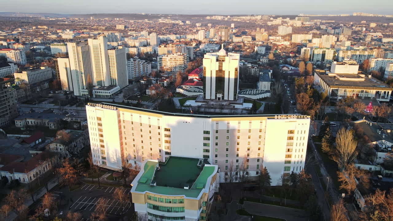 Aerial drone view of Chisinau at sunset. Panorama view of the Presidency and Parliament, multiple buildings in city center, roads with moving cars, bare trees. Moldova