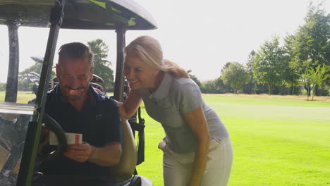 mature couple playing round on golf together sitting in buggy with score card