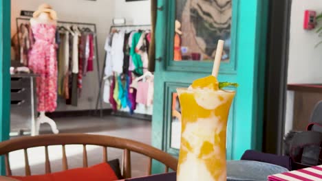 a vibrant cocktail sits on a table in a stylish resort lobby, with colorful clothing racks in the background