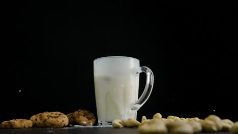 static shot of a glass filled with oat milk on the side are cookies and cashew nuts