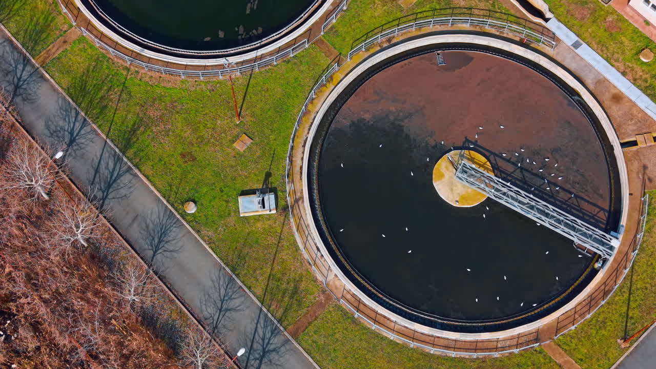 Top down view of two circular clarifiers in sewage facility. Overhead drone shot showing two large circular sedimentation tanks connected by concrete channels in sunlight