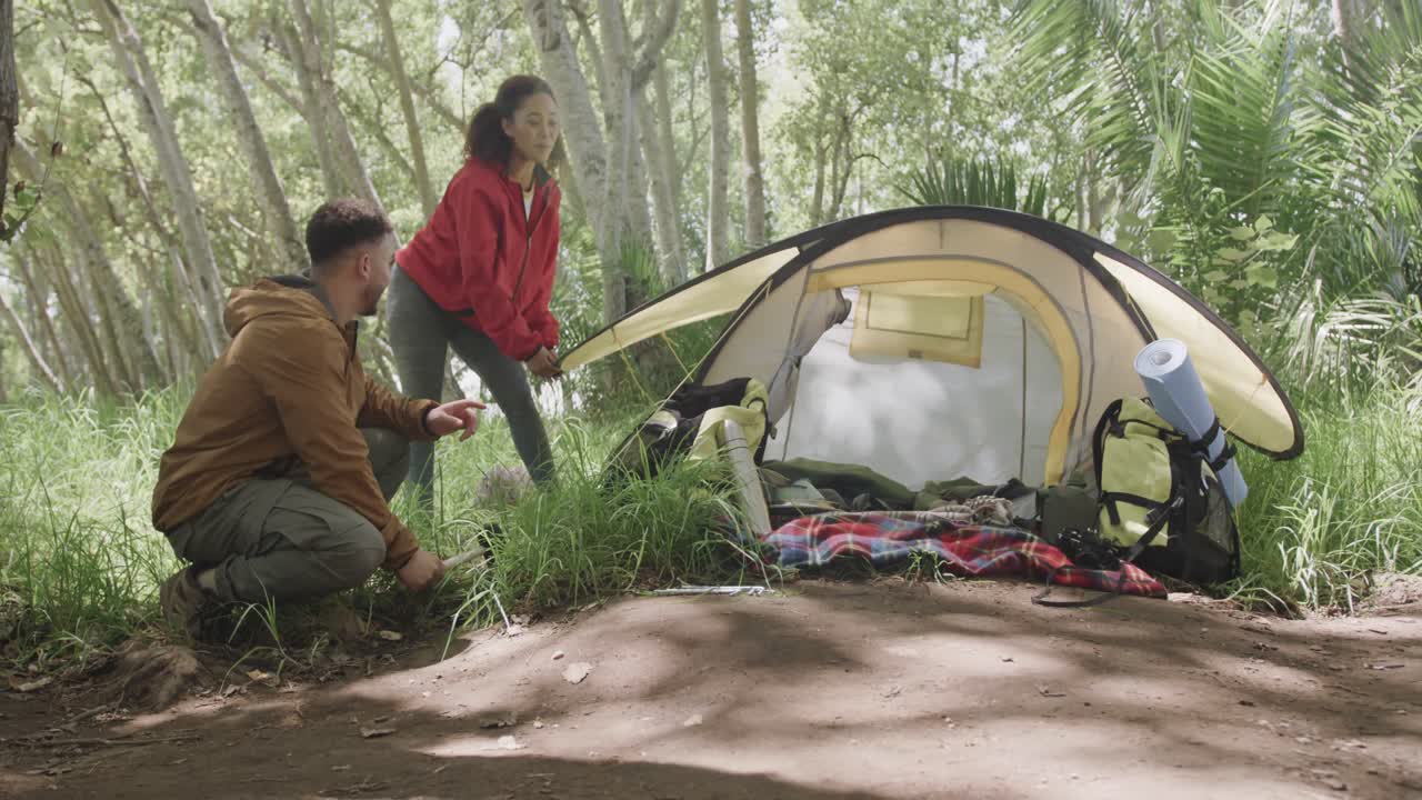 행복한 아프리카계 미국인 커플이 숲에서 천천히 텐트를 짓고 있습니다.