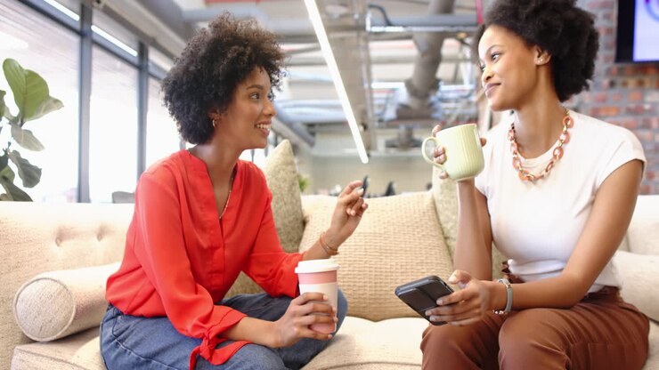 Drinking coffee, two women discussing business ideas while looking at smartphone