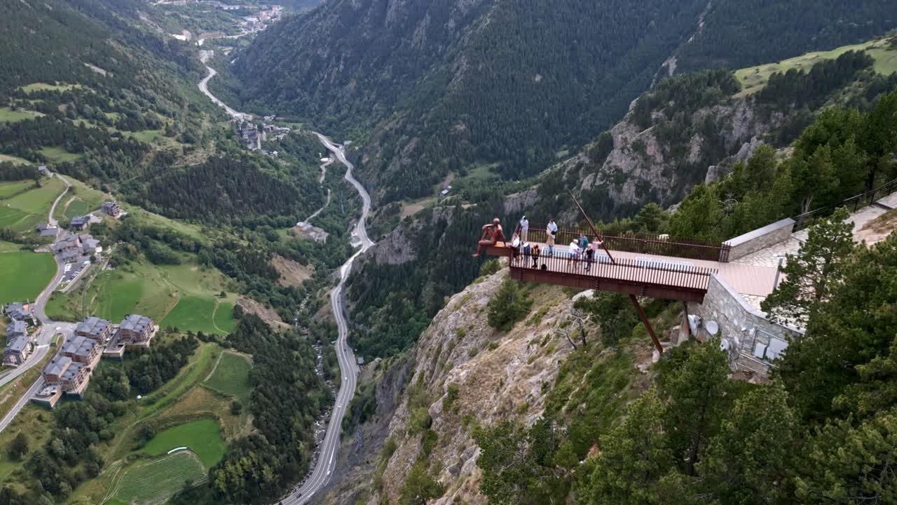 mirador colgante en una montaña en andorra, con una estatua y gente moviéndose y la ciudad se ve al fondo