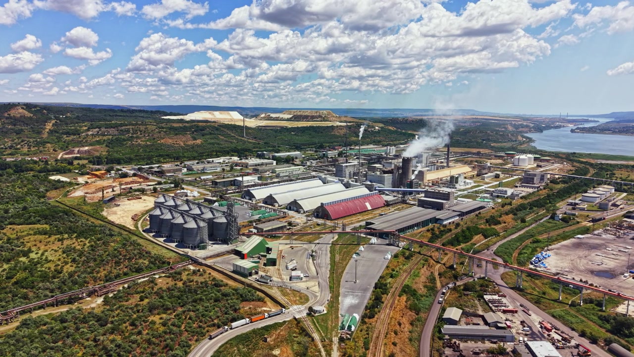 Factory and industrial area by the river with green hills and clouds during daytime in a clear sky