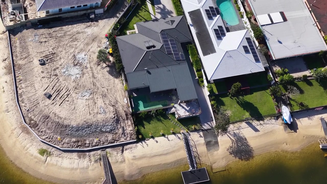 High-angle drone shot reveals upscale canal homes and a vacant lot under development.