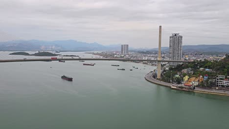 vista aérea del tráfico de automóviles en el puente de bai chay y barcos de carga navegando por el agua del río en la ciudad de ha long en un día de niebla en vietnam