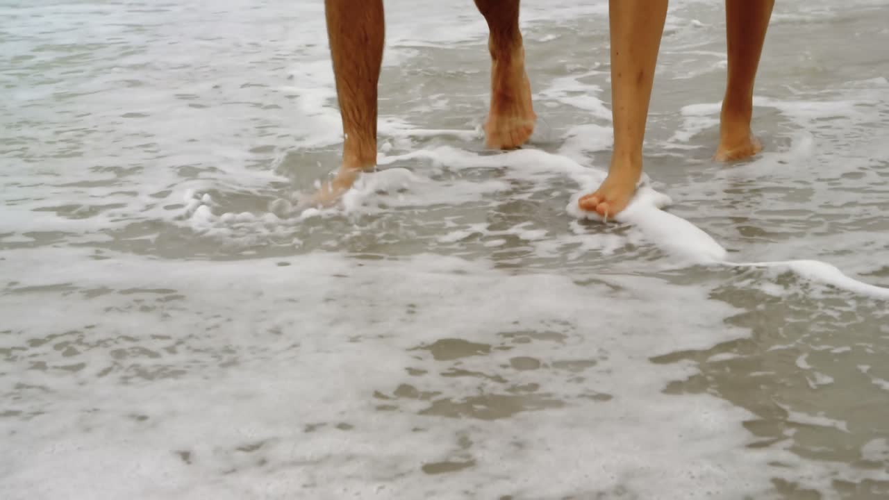 sección baja de una pareja caminando de la mano en la playa 4k