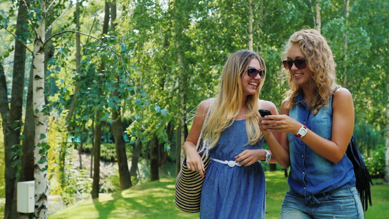 друзья гуляют по парку и пользуются смартфоном