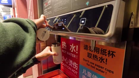 person filling cup at hot water machine