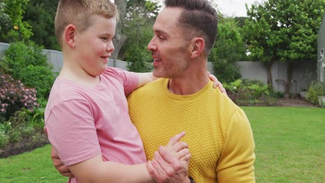 feliz padre caucásico con su hijo abrazando y llevando en el jardín