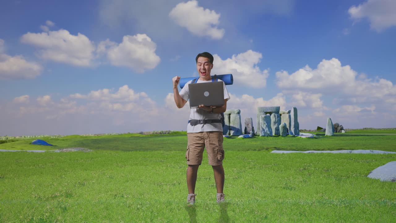 Full Body Of Asian Male Hiker With Mountaineering Backpack Looking At A Laptop And Screaming Goal Celebrating The Success While Traveling In Stonehenge