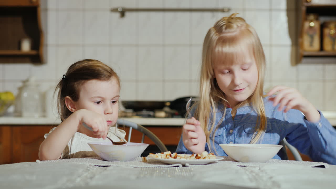 Due bambine di 5 e 7 anni mangiano la zuppa con appetito. Video 4K.