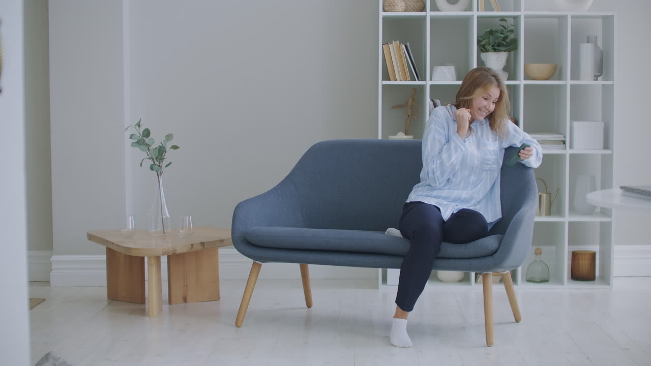 행복한 사업가 여성의 초상화 가정 사무실에서 휴대 전화에서 성공을 즐기십시오. 클로즈업 즐거운 소녀가 슬로우 모션으로 전화로 좋은 소식을 읽습니다. 아파트에서 전화로 승리를 축하하는 놀라운 여성.