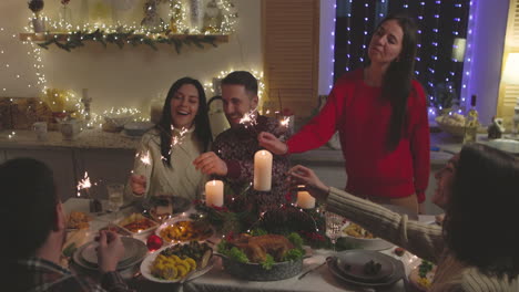 grupo de amigos felices divirtiéndose con bengalas durante la cena de navidad en casa