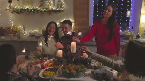 group of happy friends having fun with sparklers during christmas dinner at home