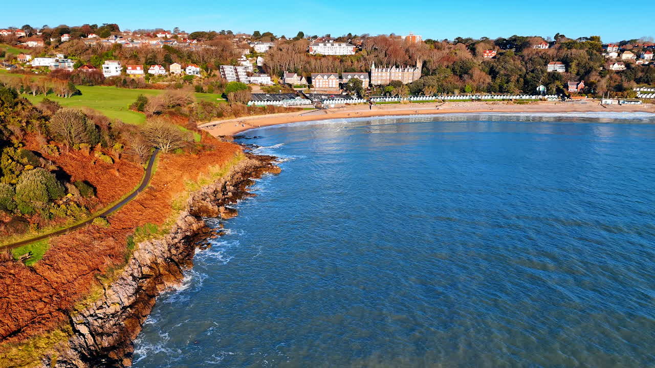 La luce intensa del sole illumina una scena costiera con un mix di scogliere, spiaggia ed edifici