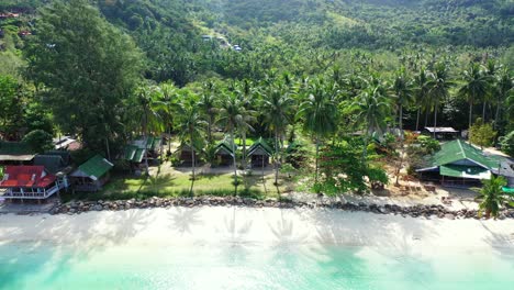 beach cabins and bungalows with sea view built on quiet shore of tropical island under palm trees on tropical island in thailand