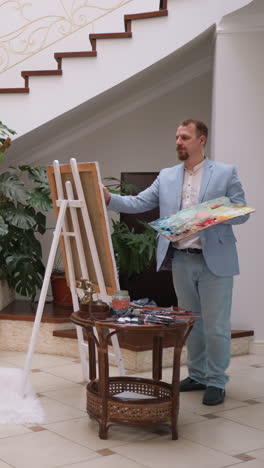 artista crea una pintura de una mujer bonita en la residencia. hermosa propietaria de la mansión en vestido rojo con rosa realiza postura para el maestro de arte en una casa de lujo