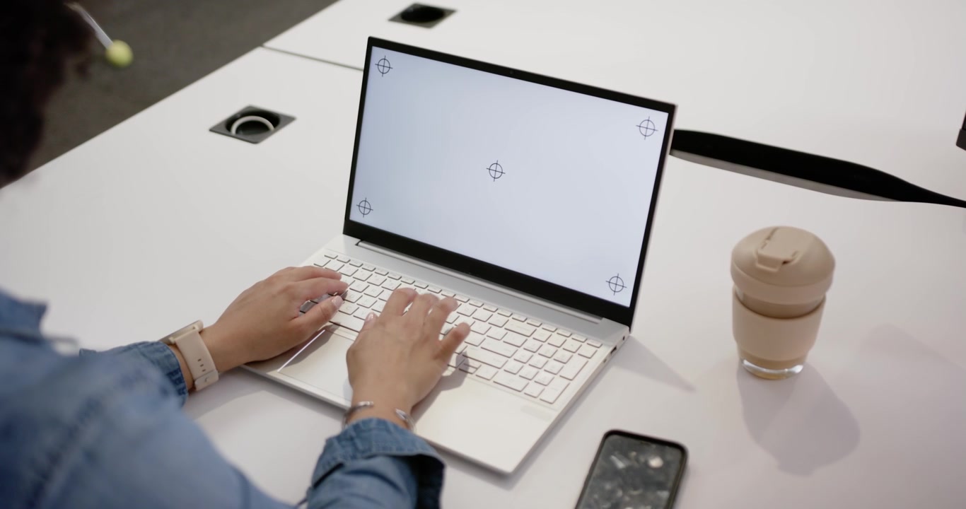 Mani che si posano sui tasti, una donna digita sul laptop a un tavolo con telefono e tazza, lavorando