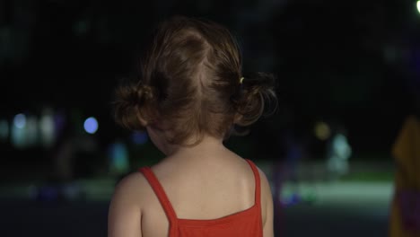 view behind beautiful toddler holding food and watching people in the park at nighttime