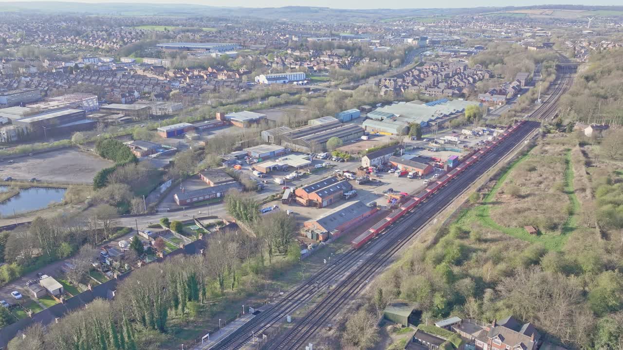 Aerial panoramic view of Chesterfield’s industrial outskirts in Derbyshire, England. A Clear morning's day. Train glides past warehouses, suburban properties and greenery.