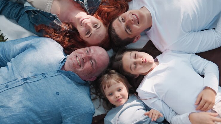 Aerial view of happy family lying down on picnic blanket with heads joined in circle, smiling under sunlight, expressing warmth, love, laughter, and togetherness in joyful outdoor moment surrounded by nature
