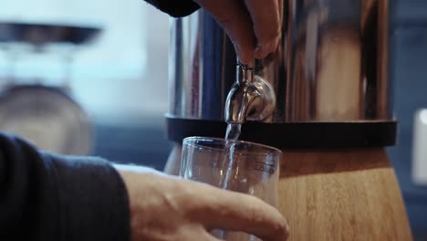 close-up of hand pouring naturally filtered water from a fountain into a glass, symbolizing natural purity, hydration, and eco-friendly refreshment