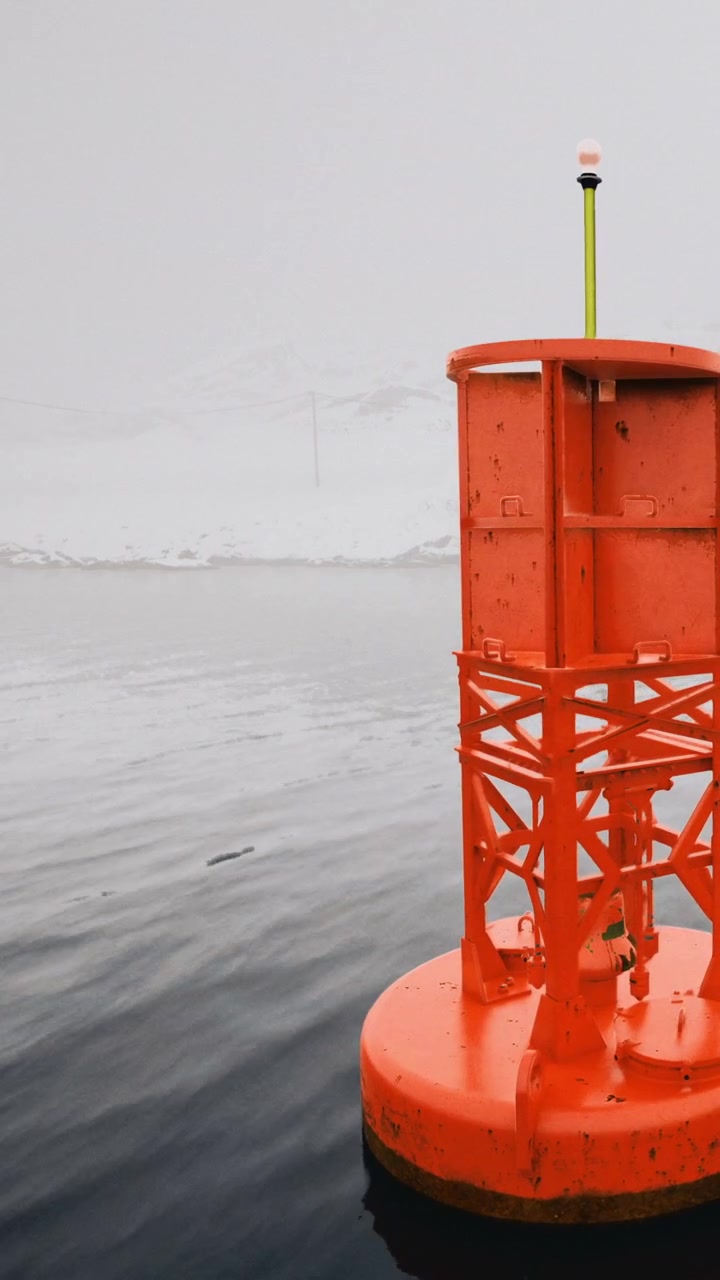 Bright orange buoy stands in still water in a foggy landscape