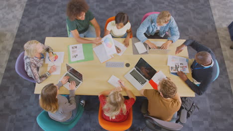 overhead shot of university or college students sitting around table with tutors in lesson