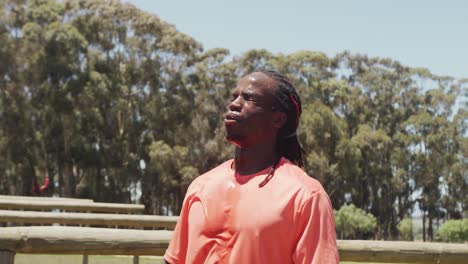 hombre afroamericano en forma con dreadlocks vertiendo agua sobre la cabeza después de hacer ejercicio en el sol
