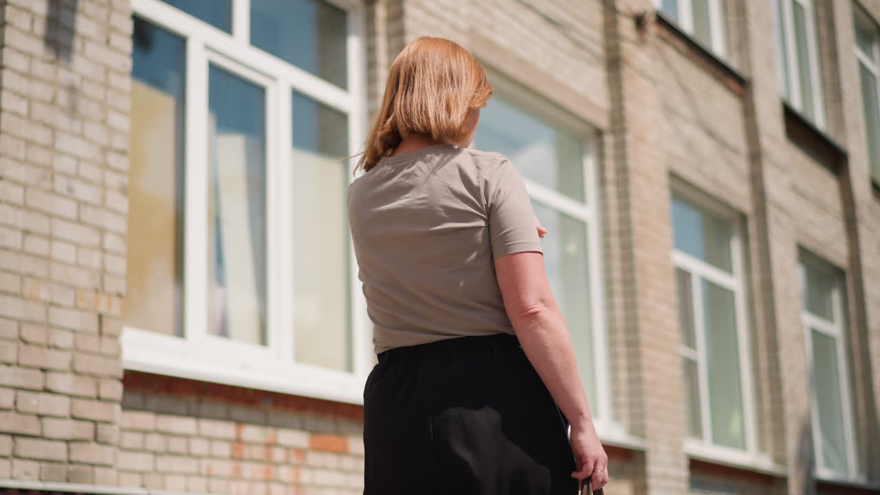 Rear view of lady walking outdoors checking wristwatch under bright sunlight, hair moving slightly in breeze, showing urgency of running late for classes, framed by trees