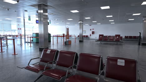 empty airport terminal with rows of red chairs and bright natural light from large windows