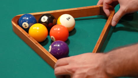 person racks 9 ball pool diamond closeup on the spot then rearranges solid and striped billiard balls on table with green felt or cloth and tightening rack with hands before lifting wooden triangle