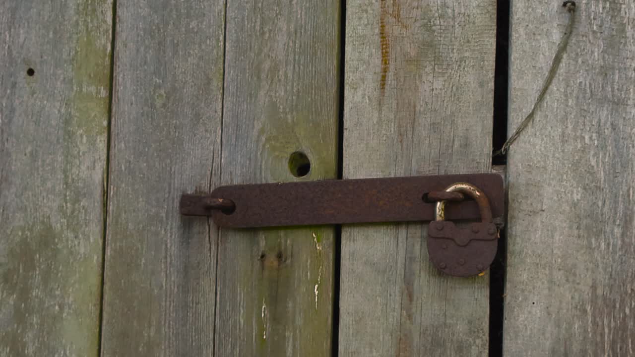Gorgeous close up or closeup footage of an old rusty and vintage padlock that is brown and orange colored and is locked in front of an old barn or shed door in the outdoors countryside during day time