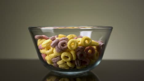 concepto de comida y desayuno. imágenes de stock. primer plano de coloridos anillos de copos de maíz en un cuenco de vidrio transparente en la superficie de la mesa oscura y el fondo de la pared gris.