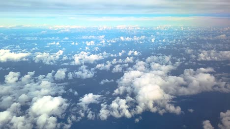 Bird's-eye-View-of-Fluffy-White-Cumulus-Clouds-In-The-Blue-Sky-Seen-Through-Airplane-Window-Above-Vast-Ocean-Underneath