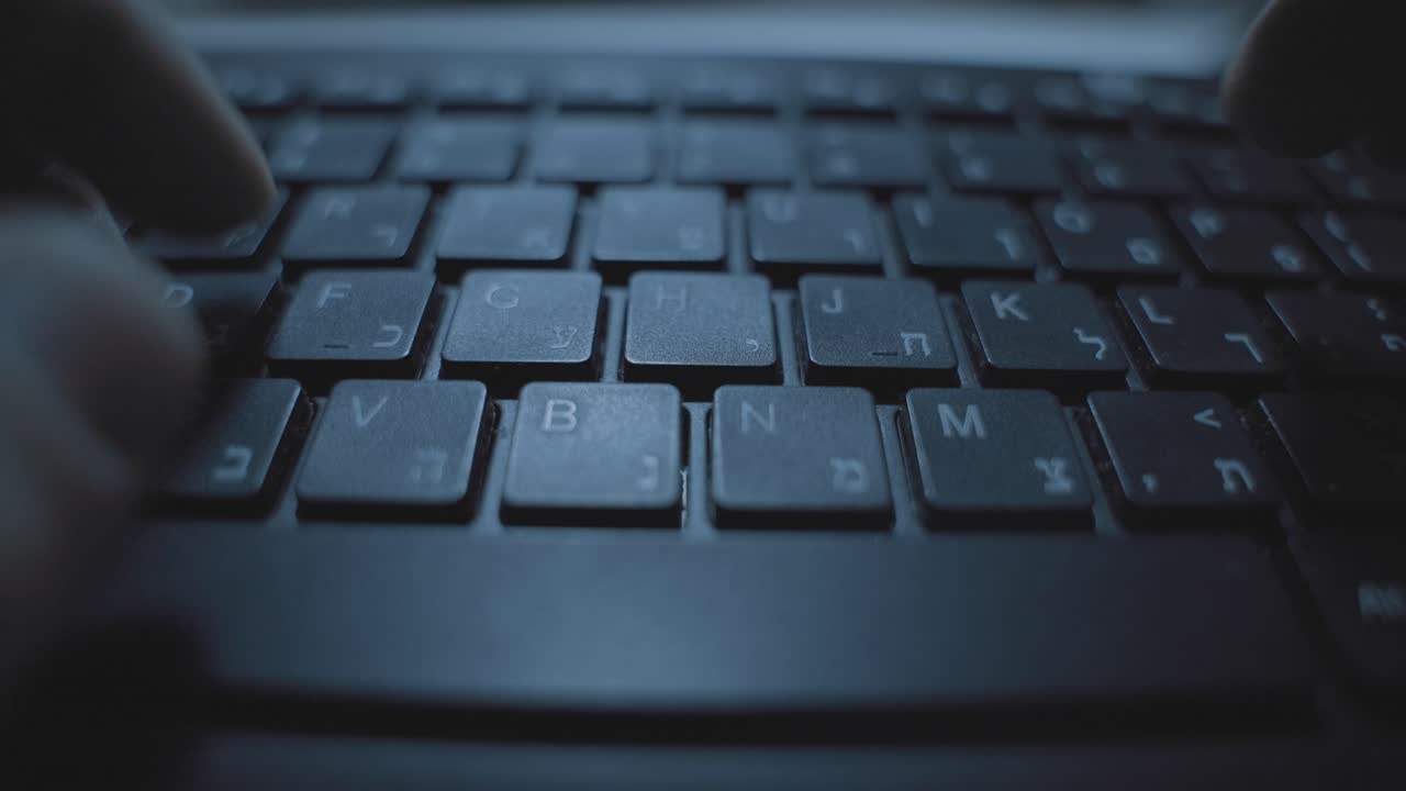 Hands typing fast on computer keyboard with Hebrew letters. Hacker or spy writing memo or sending information coding program software app. Dark web desk in office working late at night. Corporate