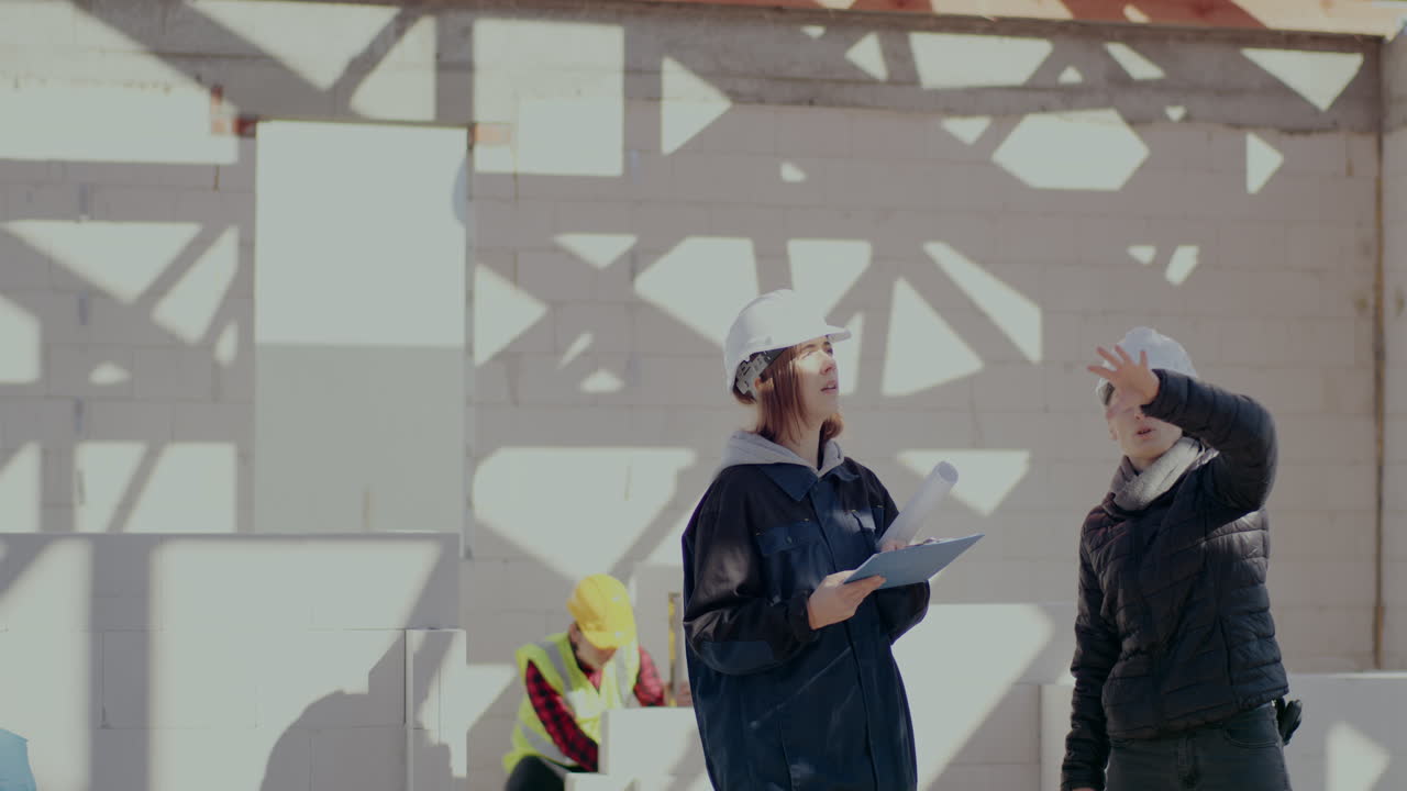 Female architect gesturing while explaining to engineer writing on clipboard at construction site