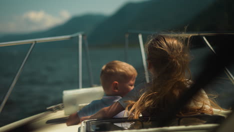 happy little boy looks at girl closing eyes with palm on motorboat on sunny day. cute children enjoy tropical cruise by modern yacht in ocean on holiday