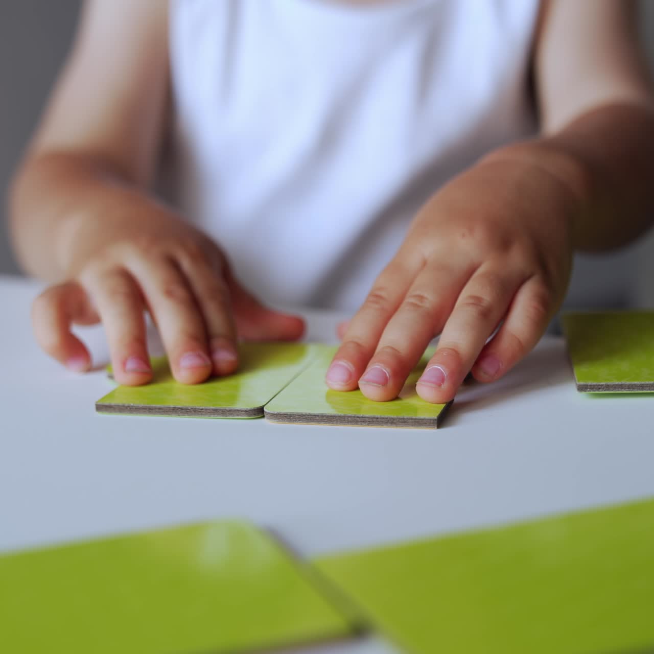 Little hands of unrecognized baby playing with puzzles. Kid moves the pieces trying to connect them properly. Close up