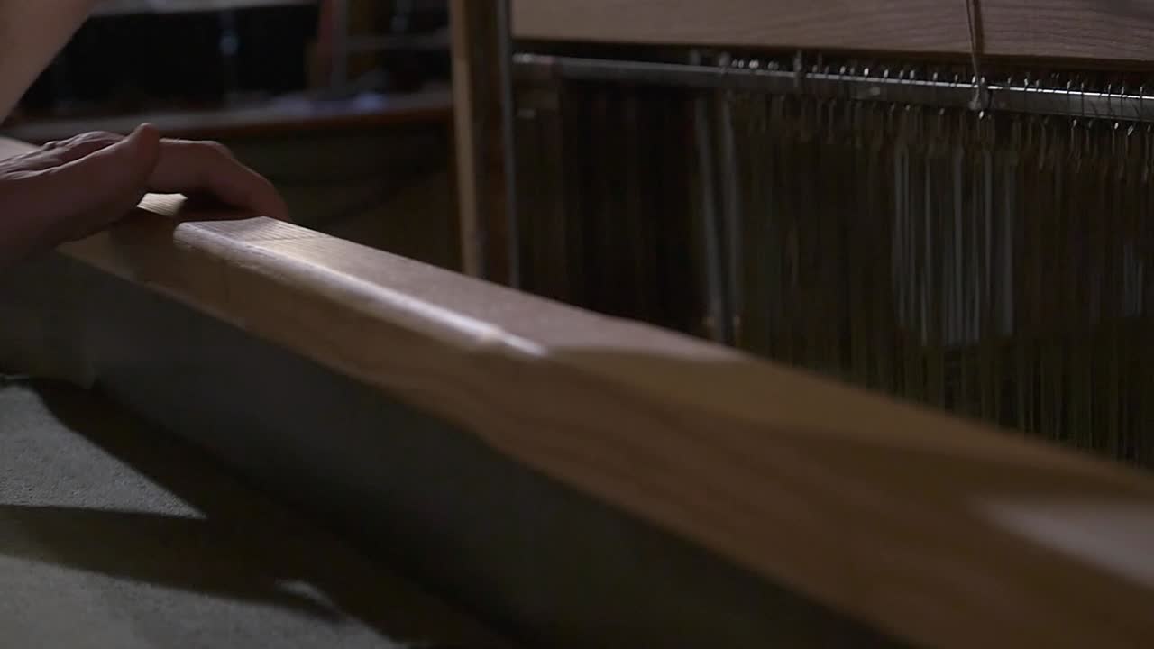 Hands handling a traditional wooden loom, interweaving olive green threads to create a fabric