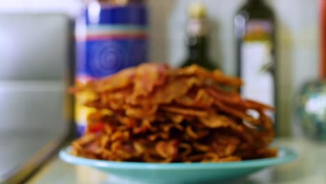 Pile-of-crispy-bacon-strips-on-plate-on-kitchen-counter,-focus-pull