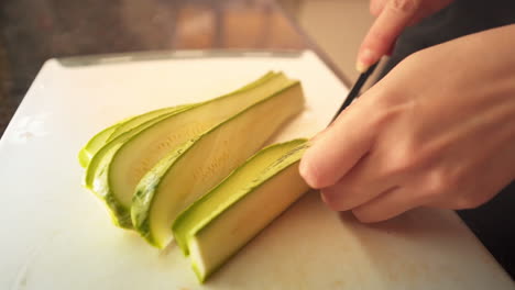 female hands slicing a green zucchini in the kitchen in slow motion