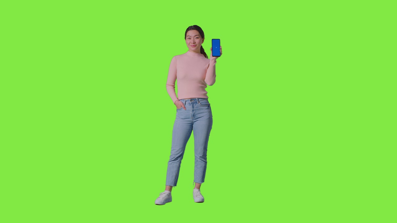 Ritratto in studio a figura intera di donna sorridente che tiene un telefono cellulare con schermo blu verso la telecamera su sfondo verde 2
