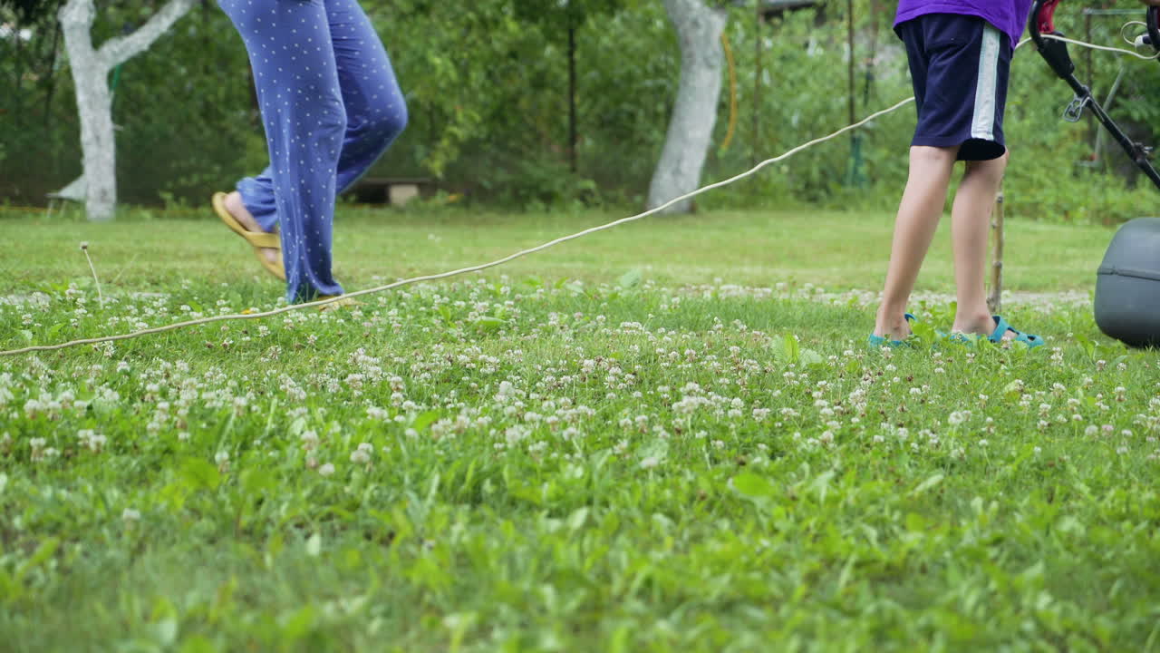 Young boy cutting the grass with a lawn mower in summer time