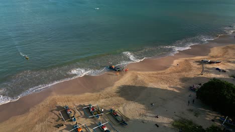 traditional fishermen return from the sea at jembaran beach in bali with their wooden boats lined along the shore captured in a peaceful drone view of coastal life in the early morning.