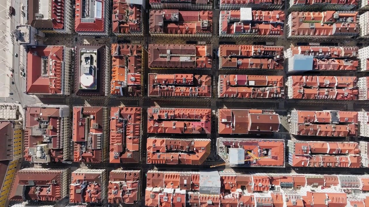 Top-down drone shot of Lisbon, Portugal. Red terracotta tiled rooftops stretch across the city. Urban aerial footage.
