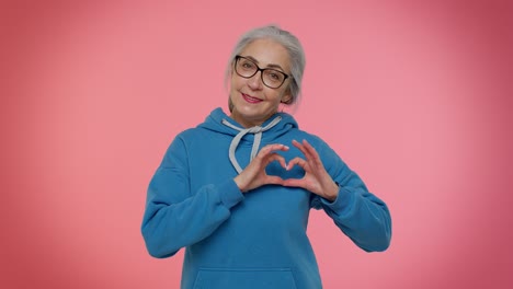 smiling senior woman makes heart gesture demonstrates love sign expresses good feelings and sympathy